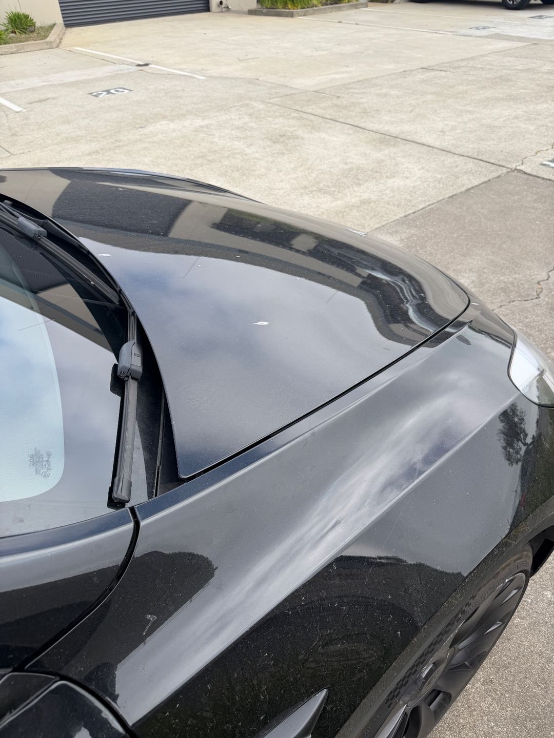 Right front fender and hood of a black Tesla Model Y before washing, dusty with specks