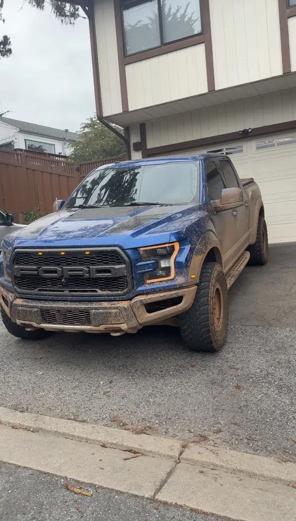 Blue Ford F-150 Raptor covered in dried mud on a driveway before a mobile detail