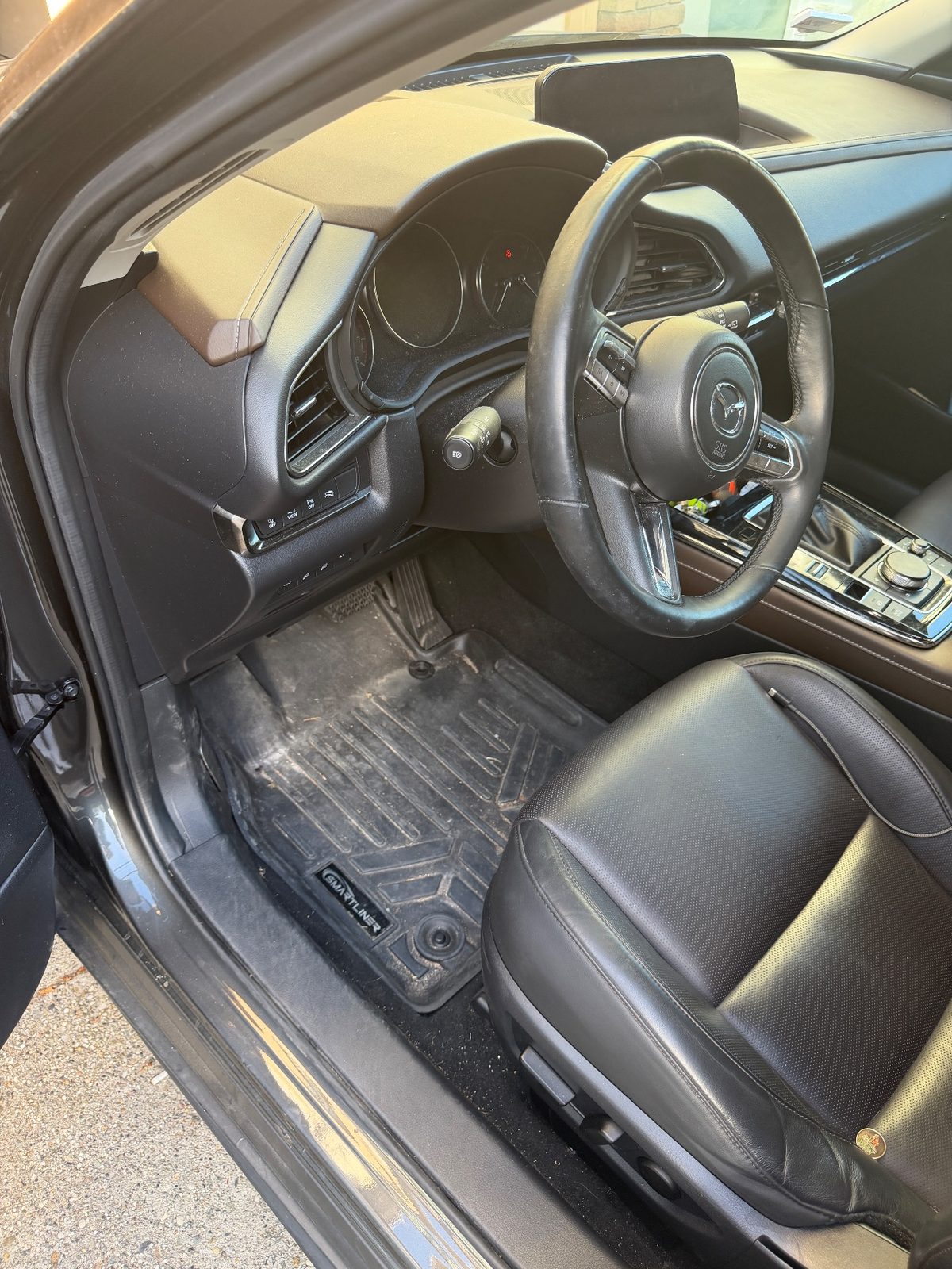Driver footwell of a grey Mazda CX-30 before detailing, floor liner caked with dirt and debris