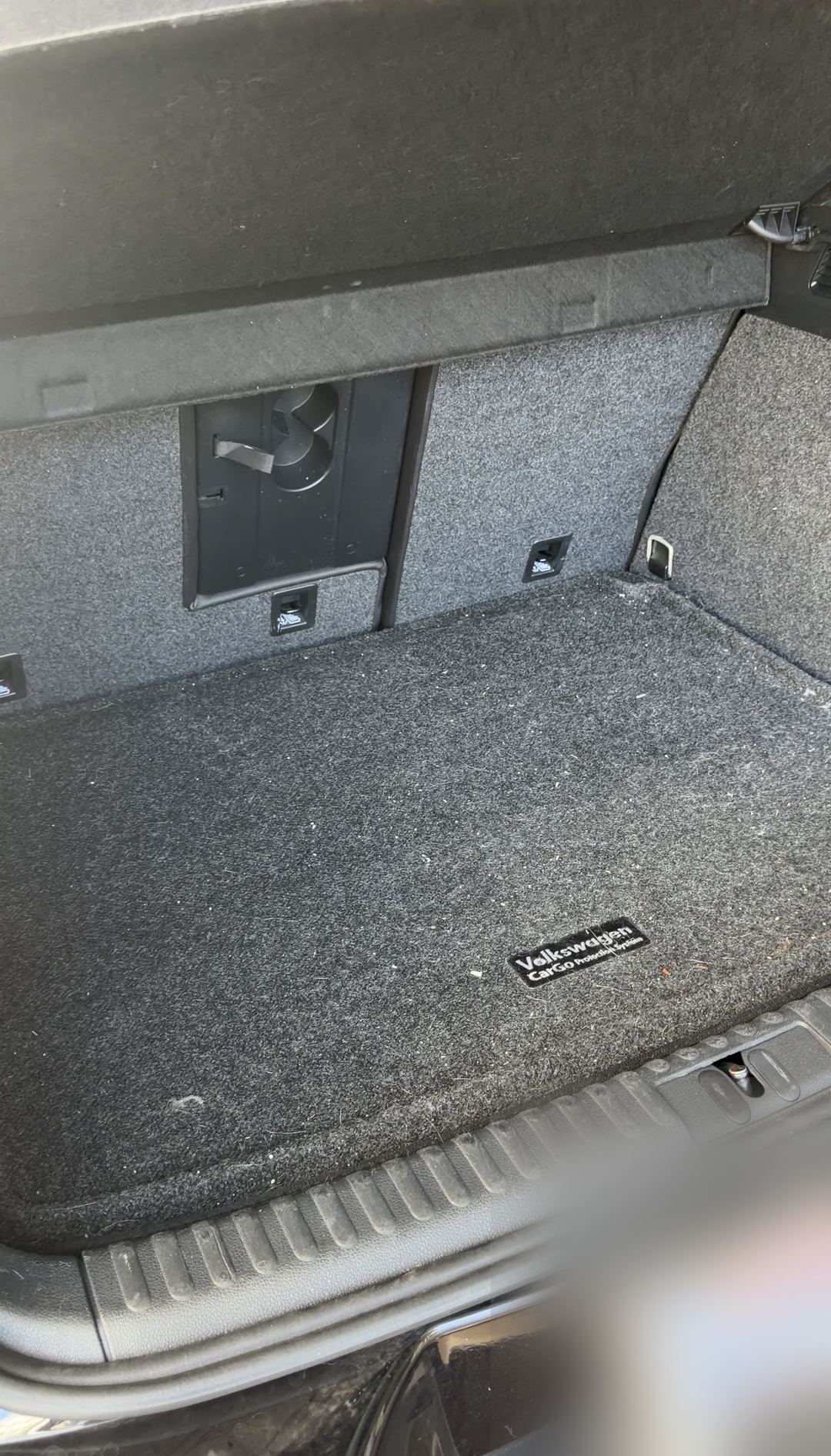 Boot of a black VW Tiguan before detailing, the Volkswagen cargo mat covered in lint and debris.