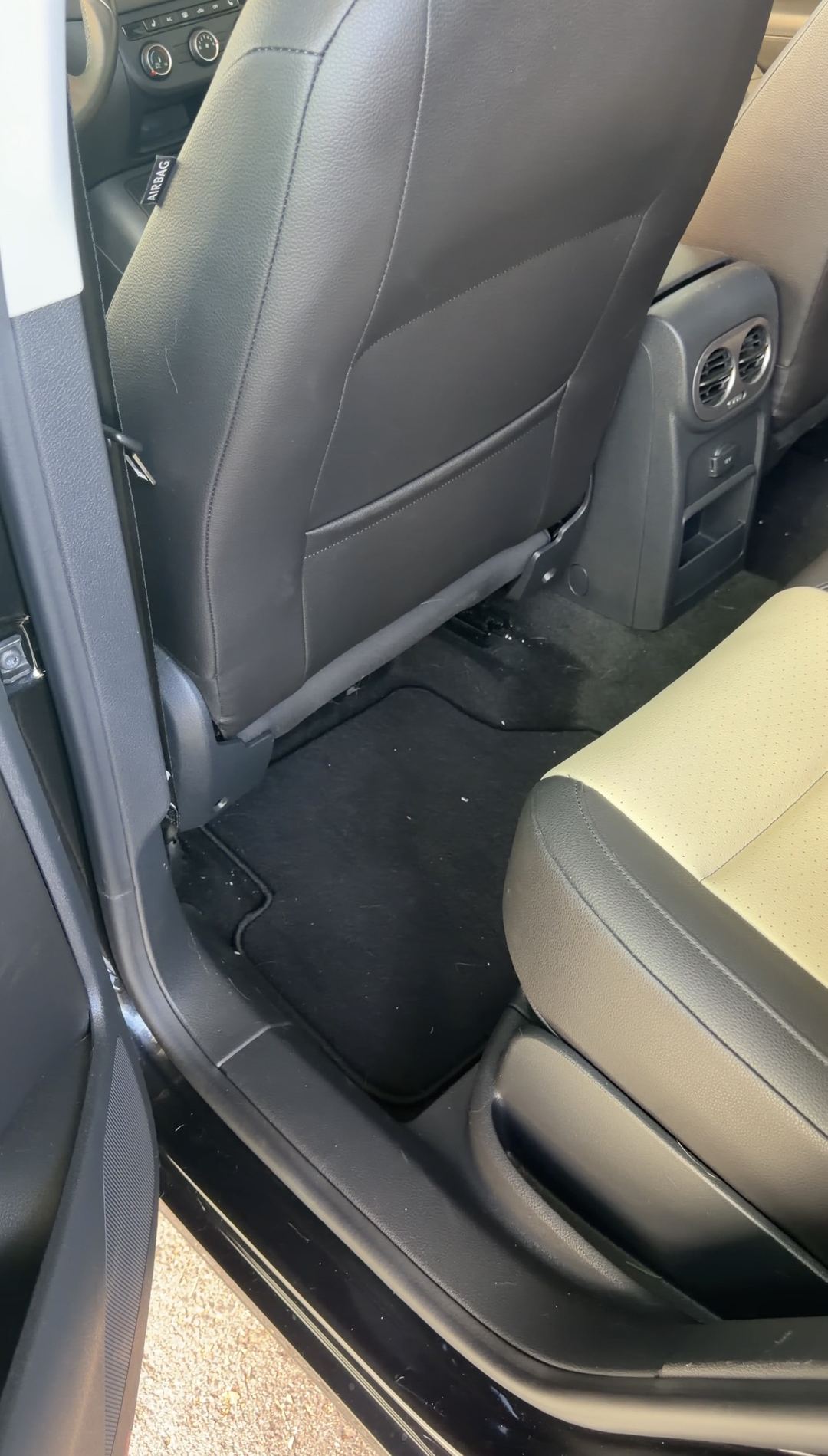 Driver-side rear footwell of a black VW Tiguan before detailing, with crumbs on the rear floor mat.