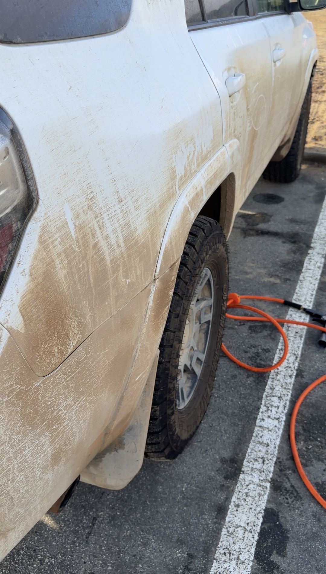 Passenger-side rear quarter panel and wheel of a white Toyota 4Runner coated in tan mud