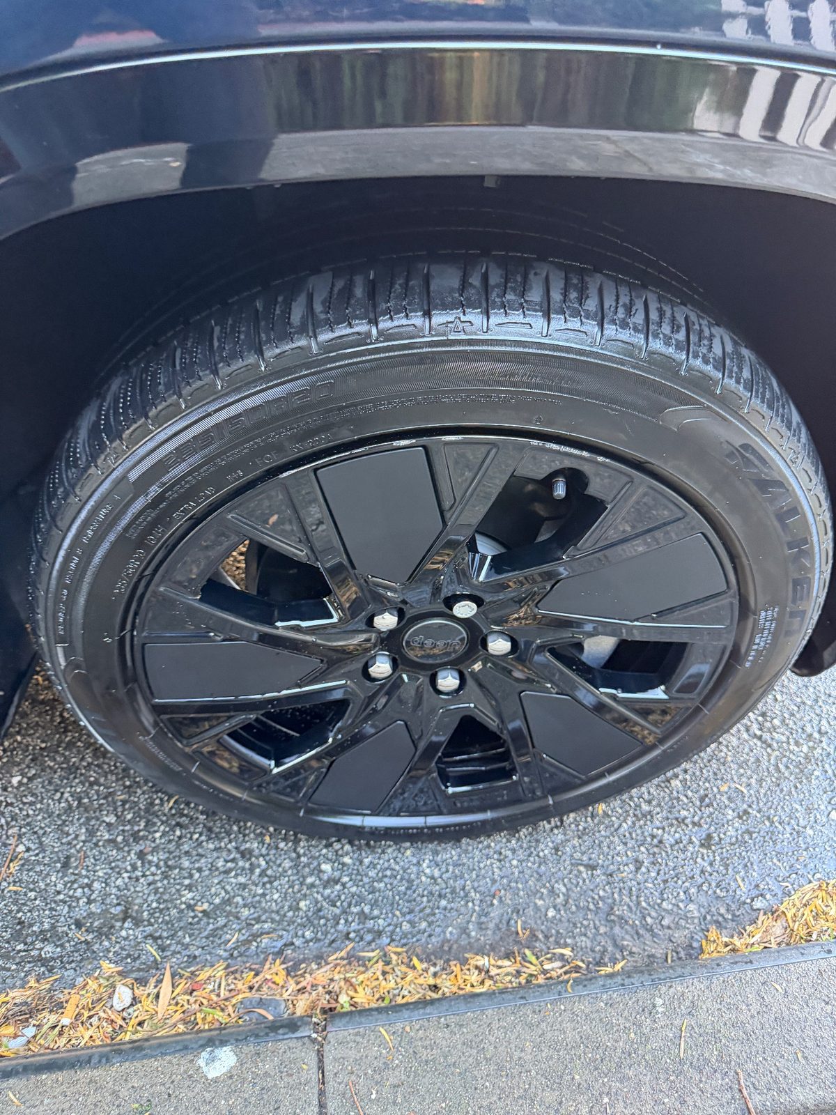 Gloss black wheel and dressed tyre of a Jeep Wagoneer S beside the kerb after detailing