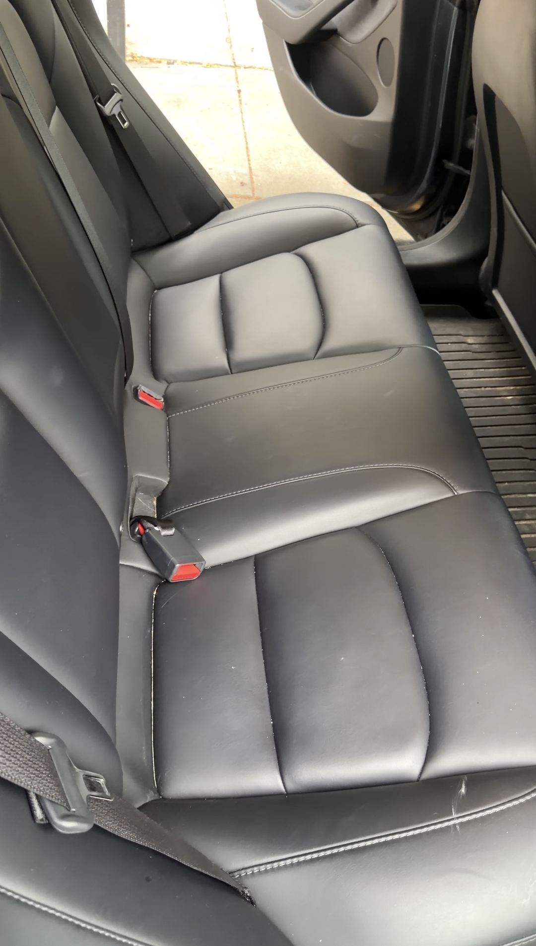 Tesla Model 3 rear bench seat before cleaning, crumbs along the seams and a dusty floor mat
