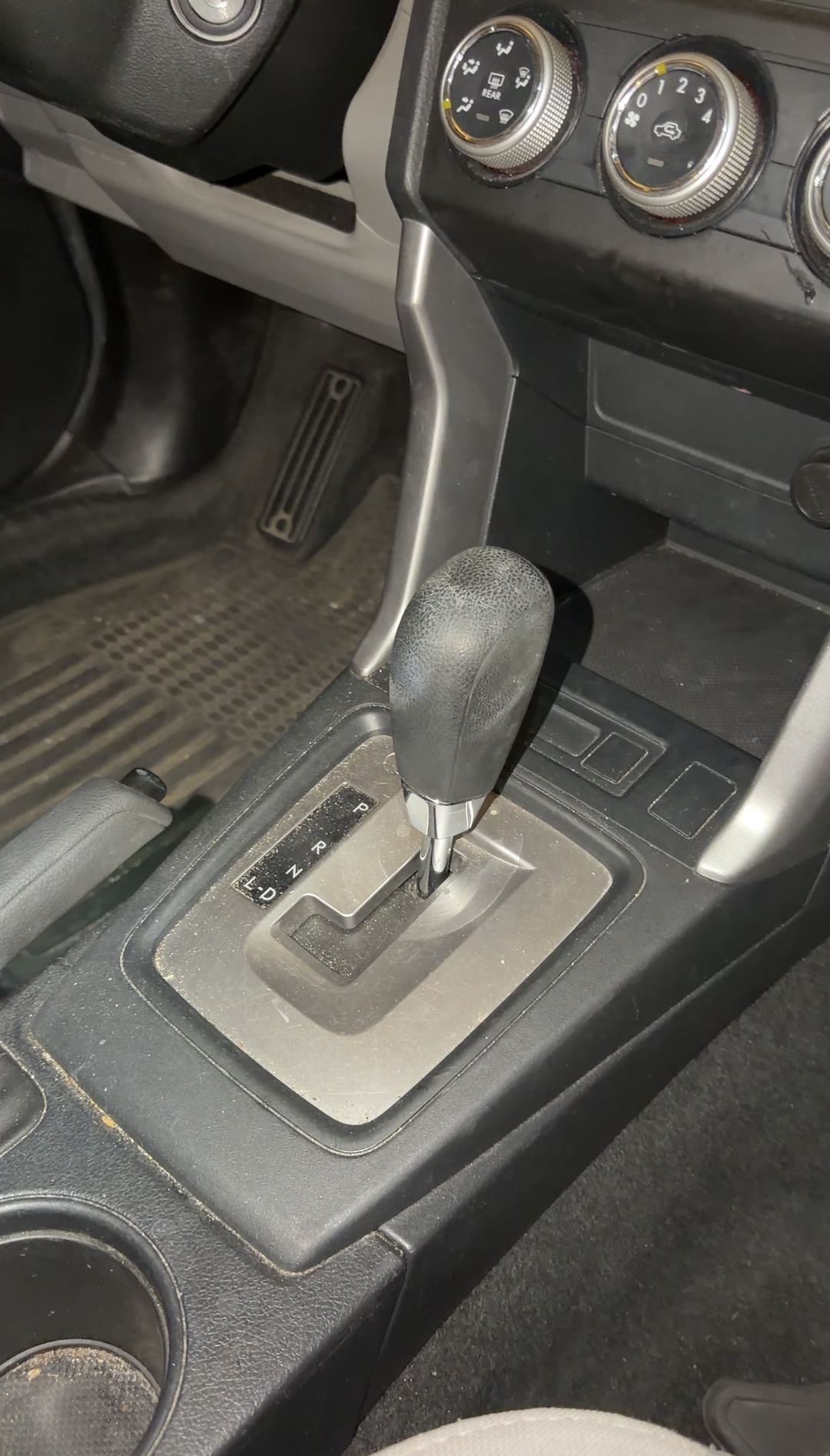 Automatic gear selector and gate surround in a blue Subaru Forester before detailing, a pale dust film over the gate plate.
