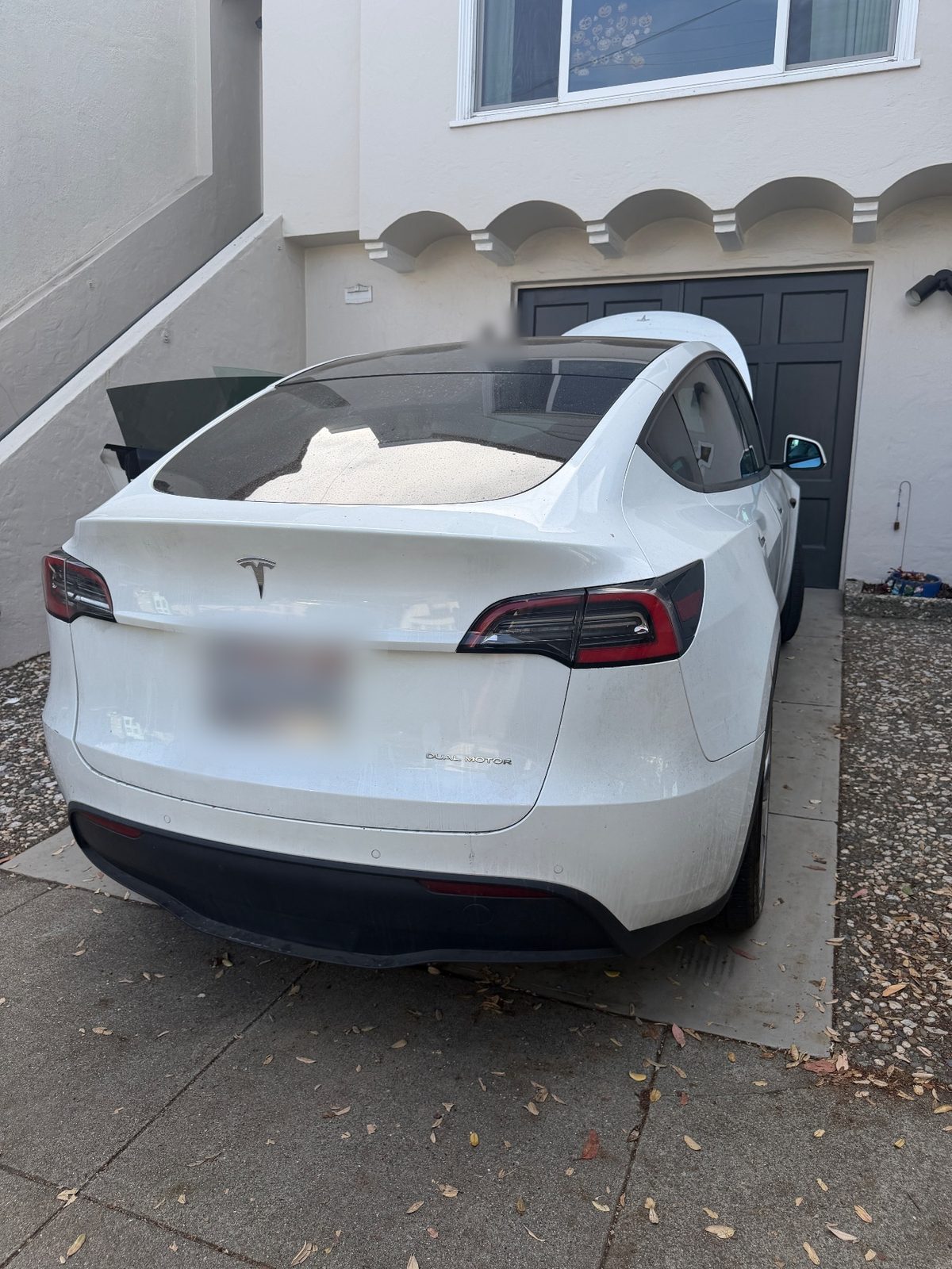 Rear of a white Tesla Model Y before detailing, with a dusty rear window and tailgate