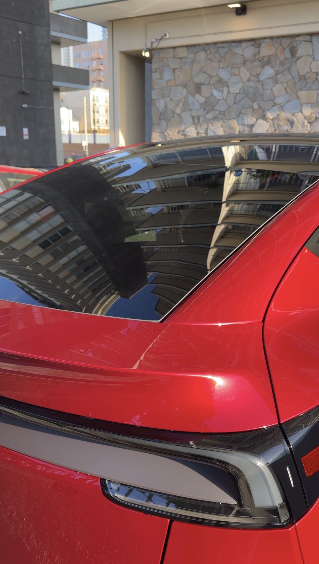 Spotless glass roof and rear glass of a red Tesla Model Y reflecting an apartment building after detailing