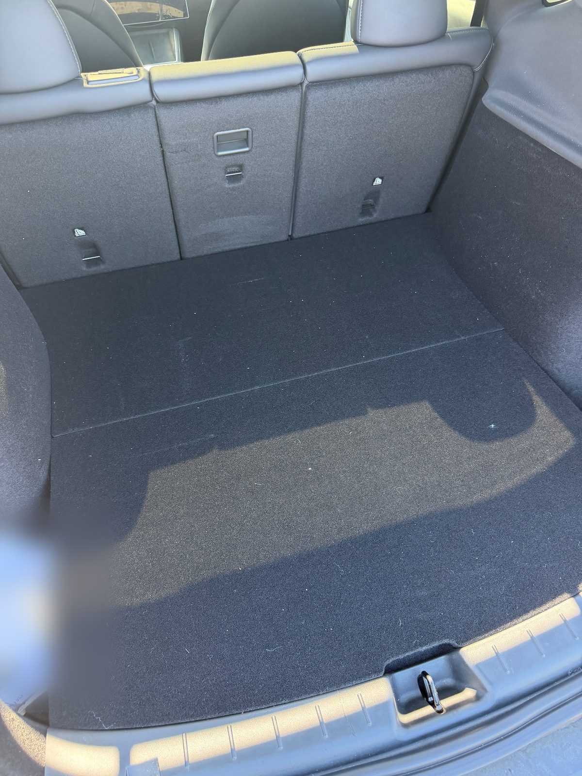 Cargo area of a white Tesla Model Y before vacuuming, lint and dust on the carpet