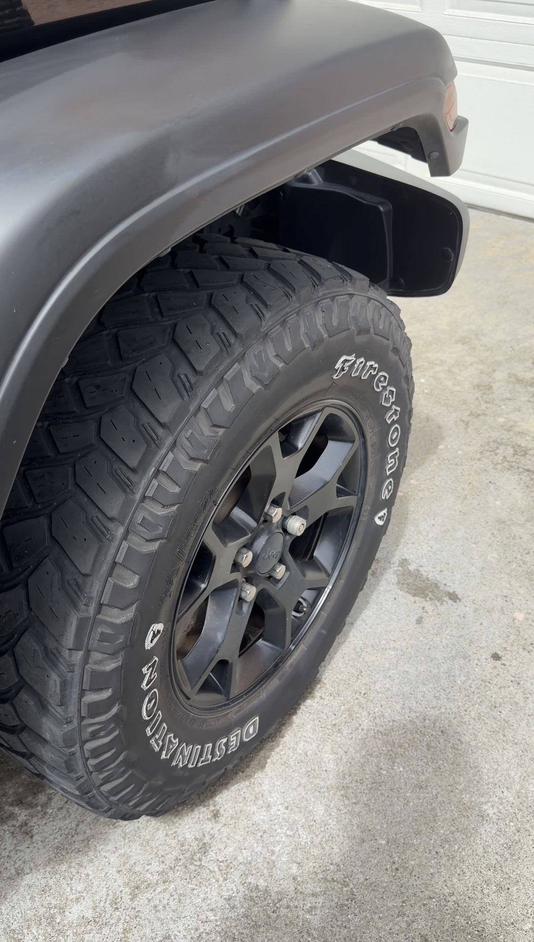 Jeep Wrangler tyre, black wheel and fender flare after cleaning, wet driveway below
