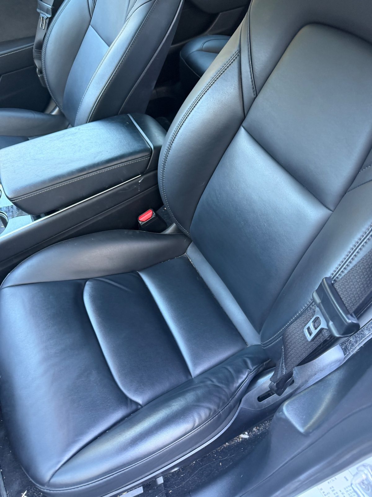 Driver seat of a white Tesla Model 3 before detailing, with lint on the seat belt and floor