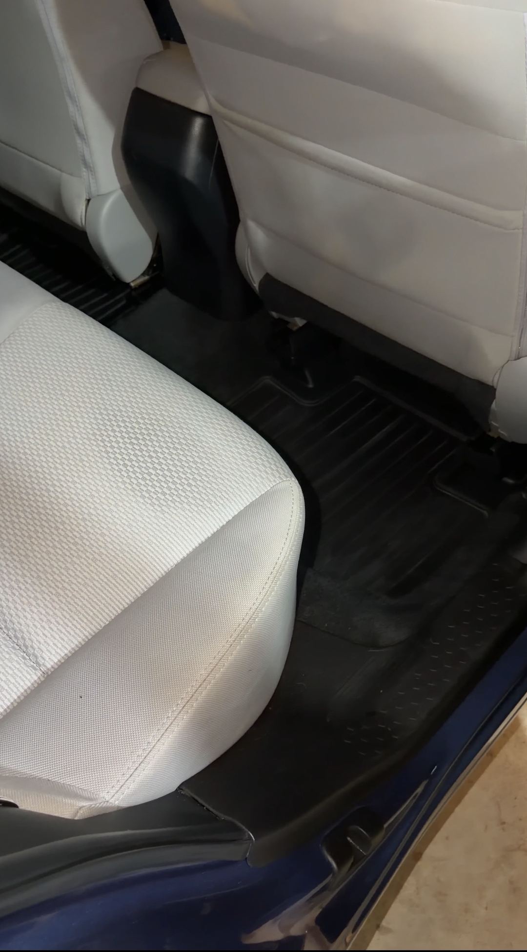 Rear passenger-side footwell of a blue Subaru Forester after detailing, the black rubber rear mat clean beside the light grey cloth bench.