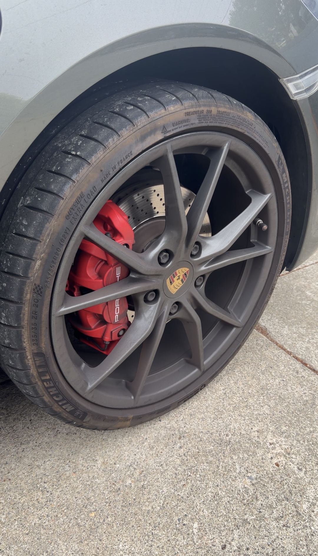 Front wheel of a Porsche 718 Cayman S shot from a three-quarter angle, spokes dulled with brake dust before cleaning.