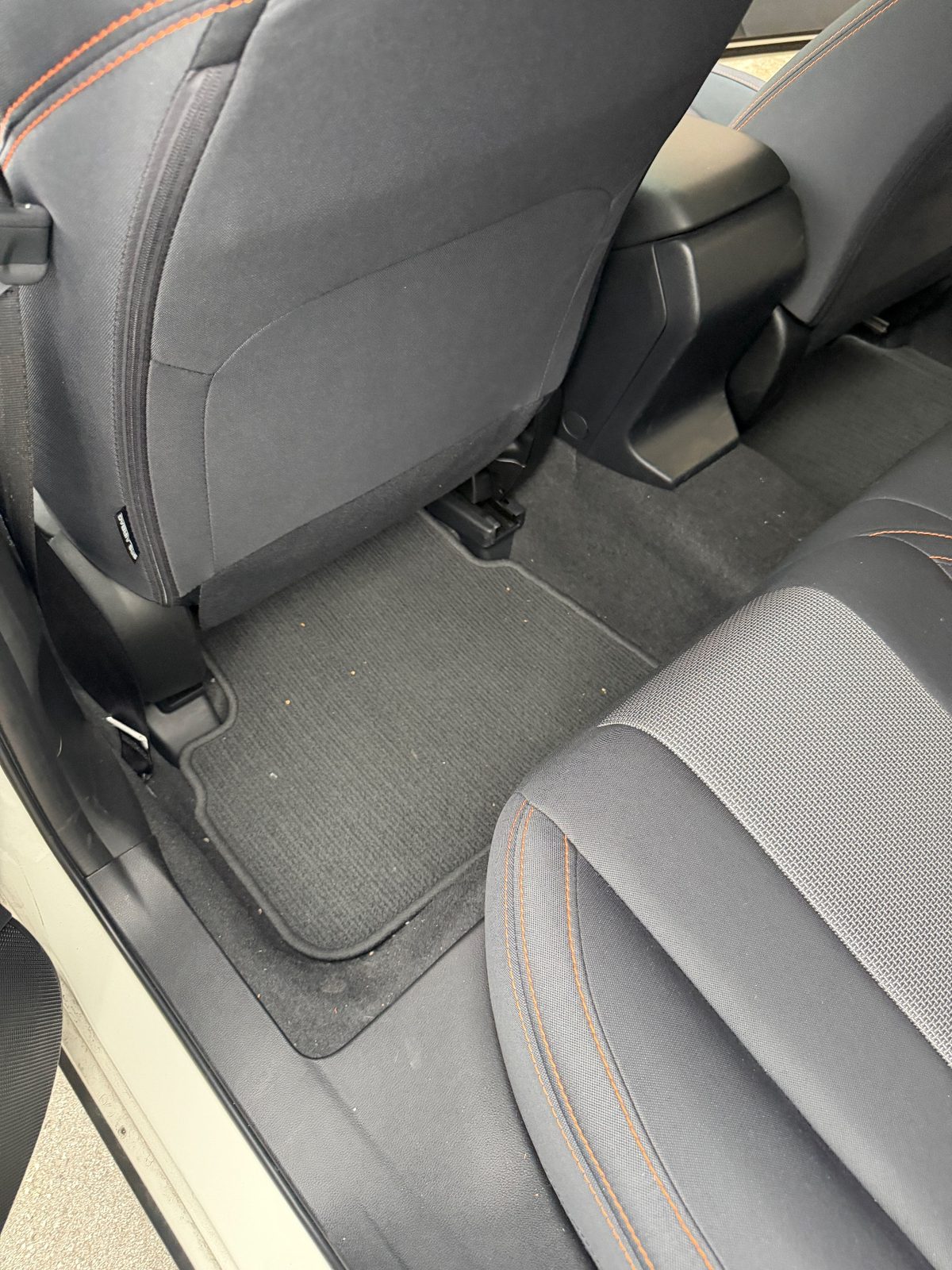 Rear footwell mat of a Subaru Crosstrek before vacuuming, crumbs and debris on the carpet