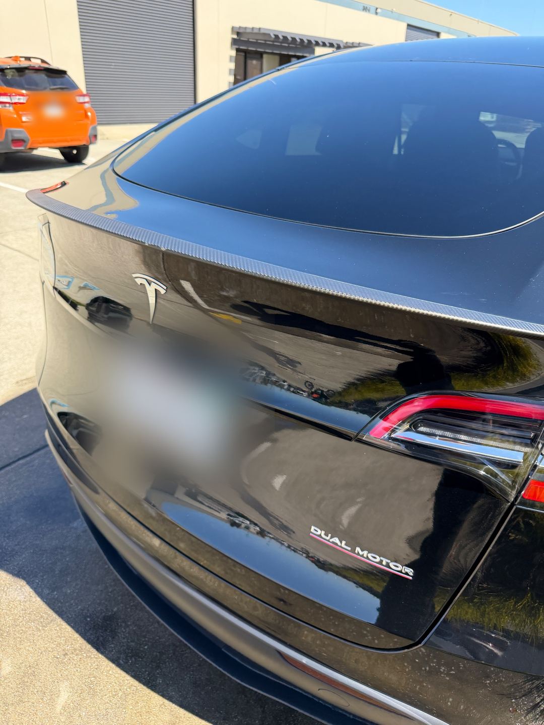 Rear hatch of a Tesla Model Y Performance with carbon spoiler and red-underlined Dual Motor badge after detailing
