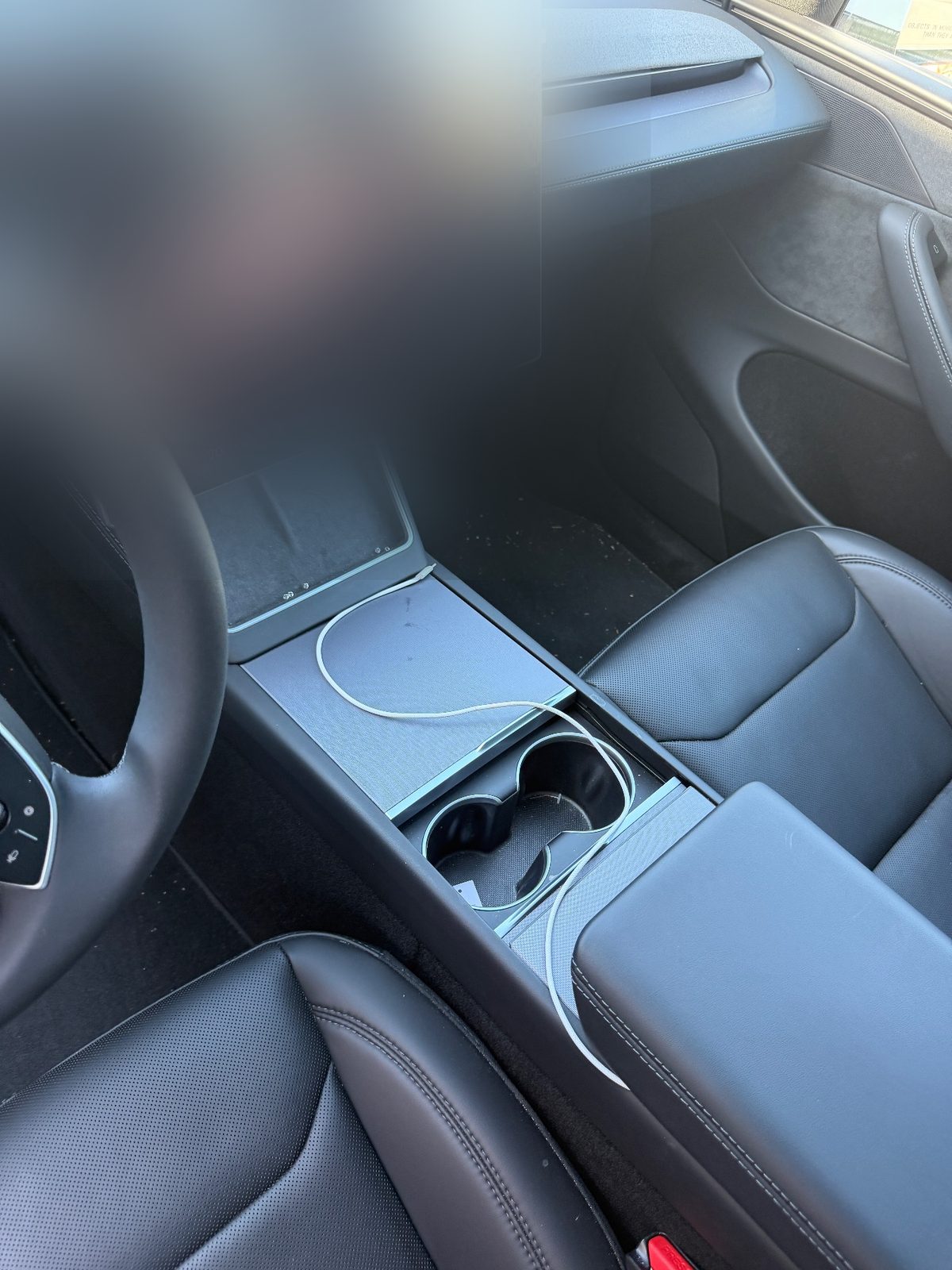 Dash and centre console of a white Tesla Model Y before detailing, cable over the console and debris on the mat