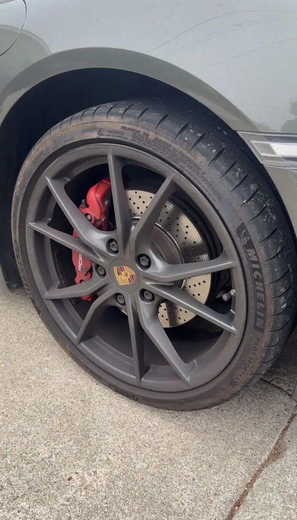 Dirty satin silver Porsche wheel with caked brake dust on the spokes and a browned tyre sidewall before cleaning.