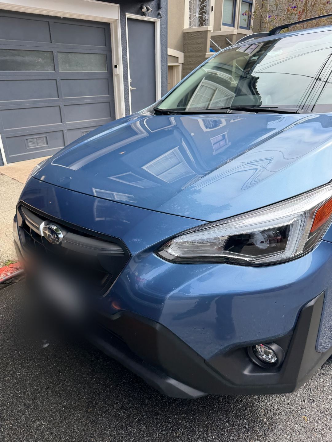 Glossy hood and front grille of a blue Subaru Crosstrek after washing, reflecting the house behind