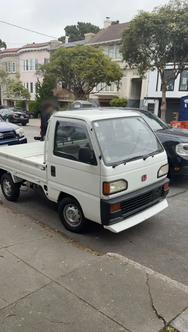 White Honda Acty flat-bed kei truck parked on a residential San Francisco street, seen from the front three-quarter before detailing.