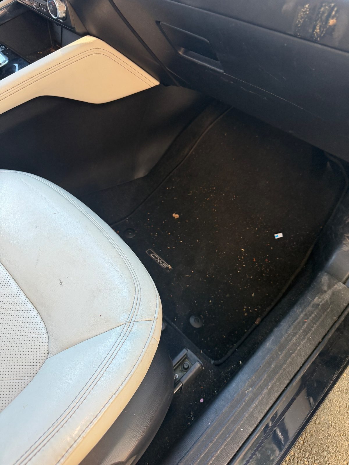 Front passenger footwell of a dark blue Mazda CX-5 before detailing, floor mat covered in crumbs and debris