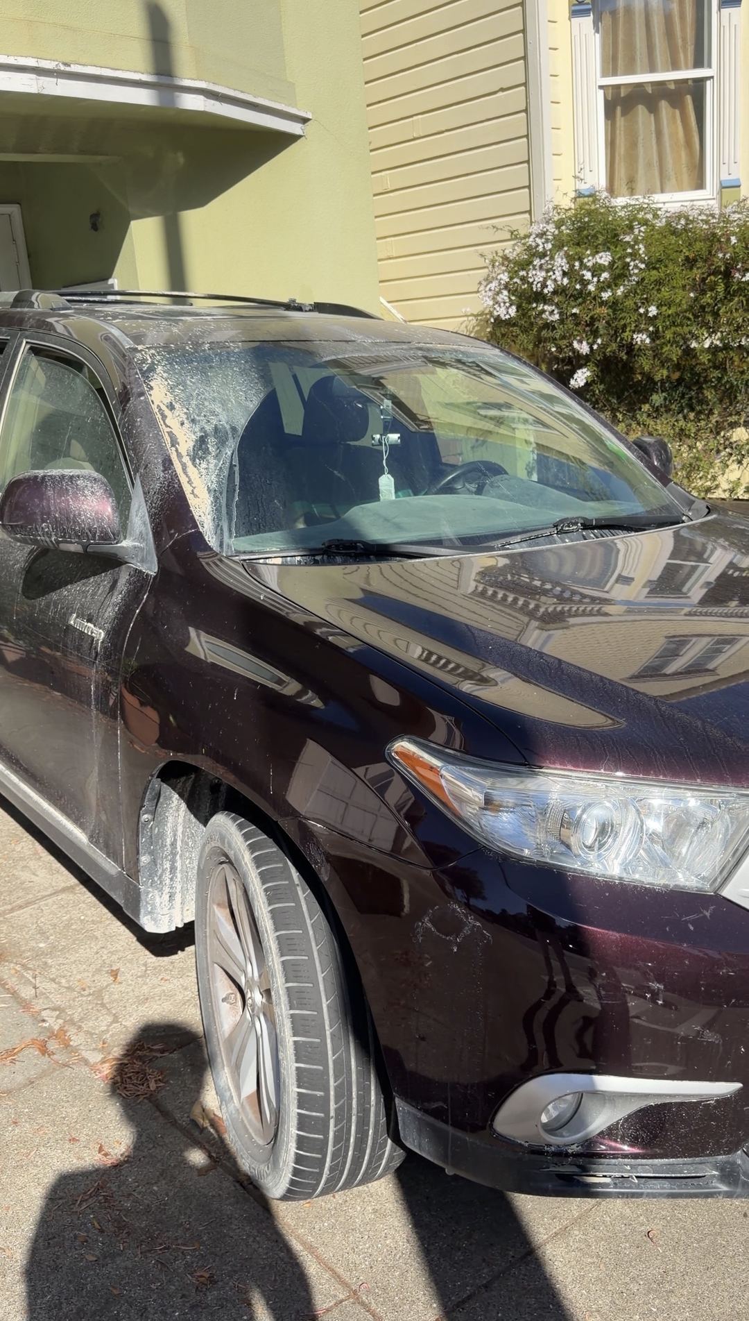 Plum Toyota Highlander coated in pale dust, with the windshield and wheel caked before cleaning