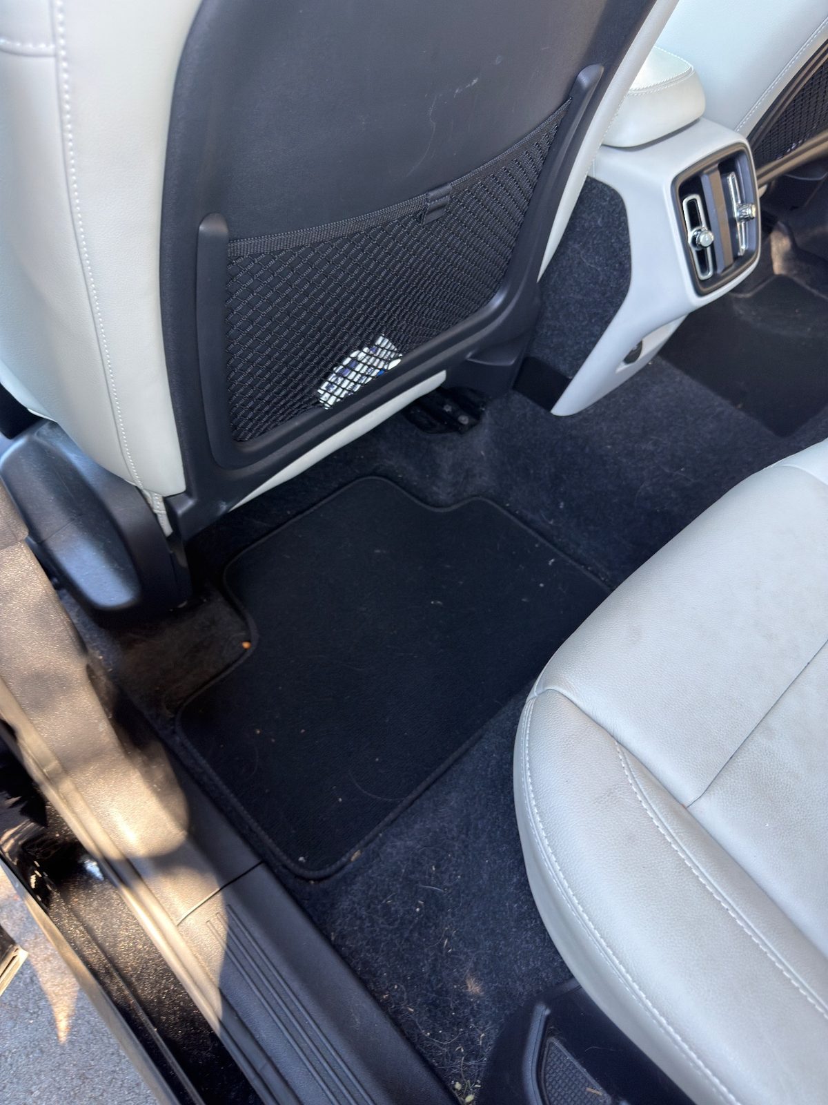 Rear footwell of a Volvo XC40 before detailing, with lint and crumbs on the black mat and carpet