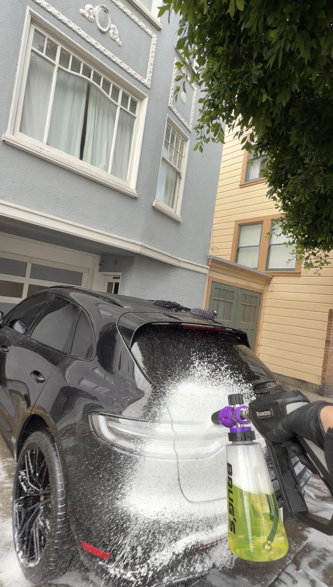 Snow foam being applied to the rear of a black Porsche Macan GTS during a mobile exterior wash in San Francisco.