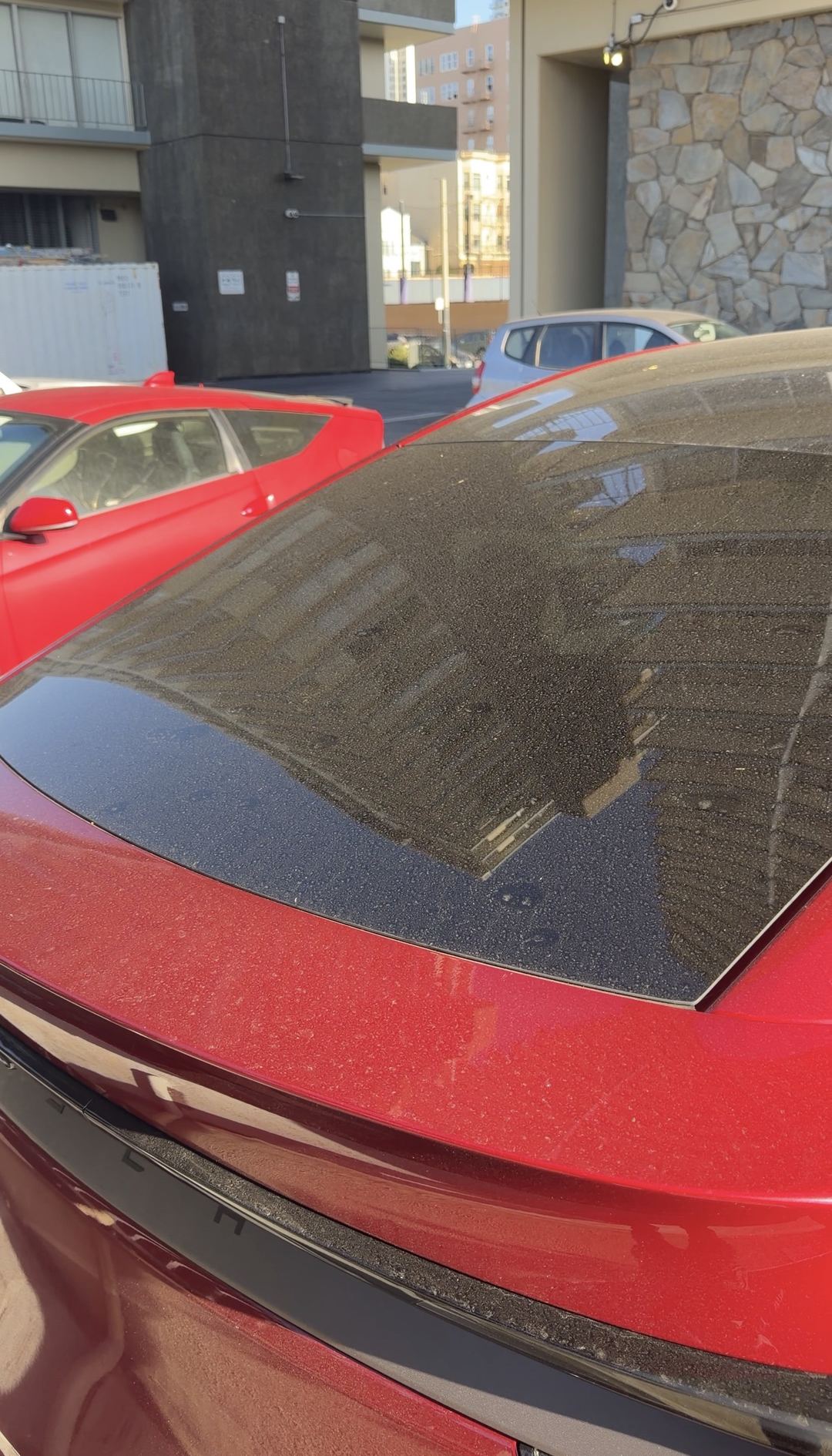 Heavy dust covering the panoramic glass roof and rear glass of a red Tesla Model Y before cleaning