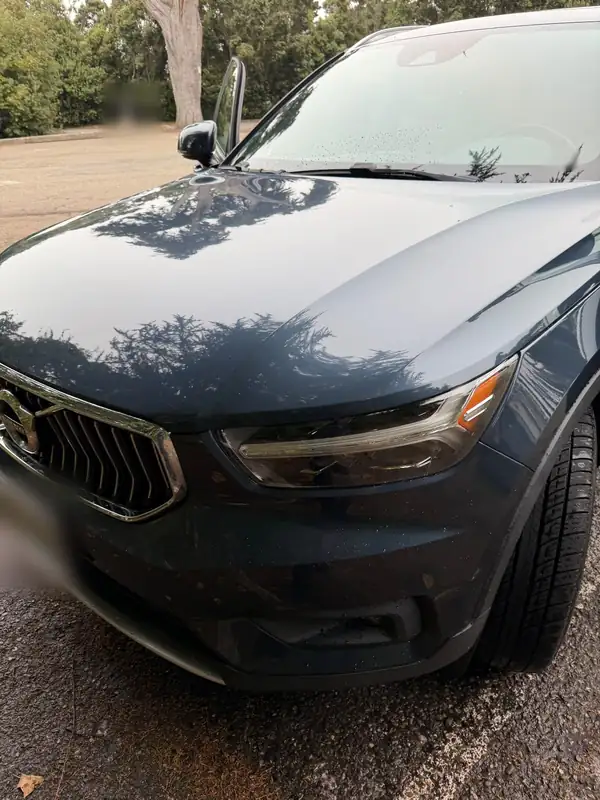 Front of a clean Volvo XC40 in a parking lot after washing, the hood showing clear tree reflections