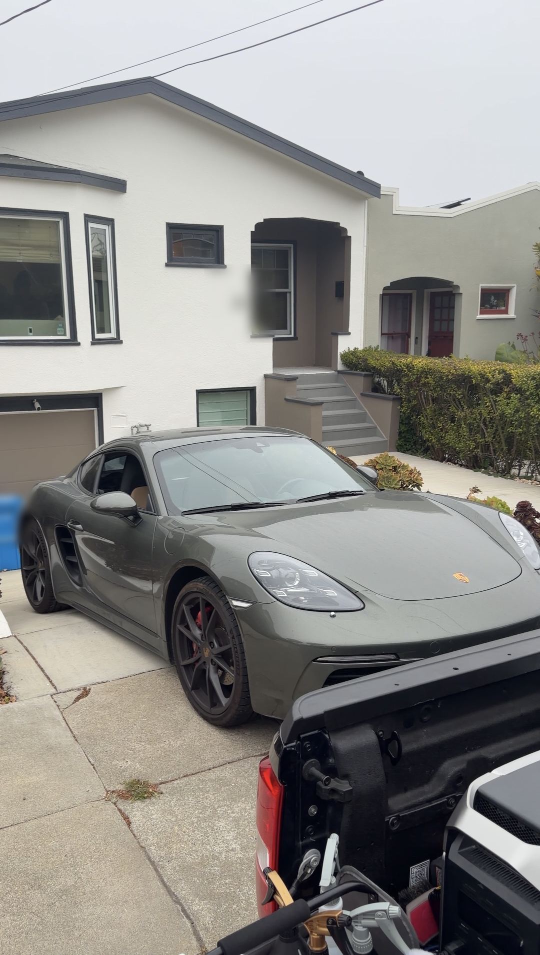 Green Porsche 718 Cayman S parked on a San Francisco driveway before a mobile detail, its paint covered in a dry dust film.