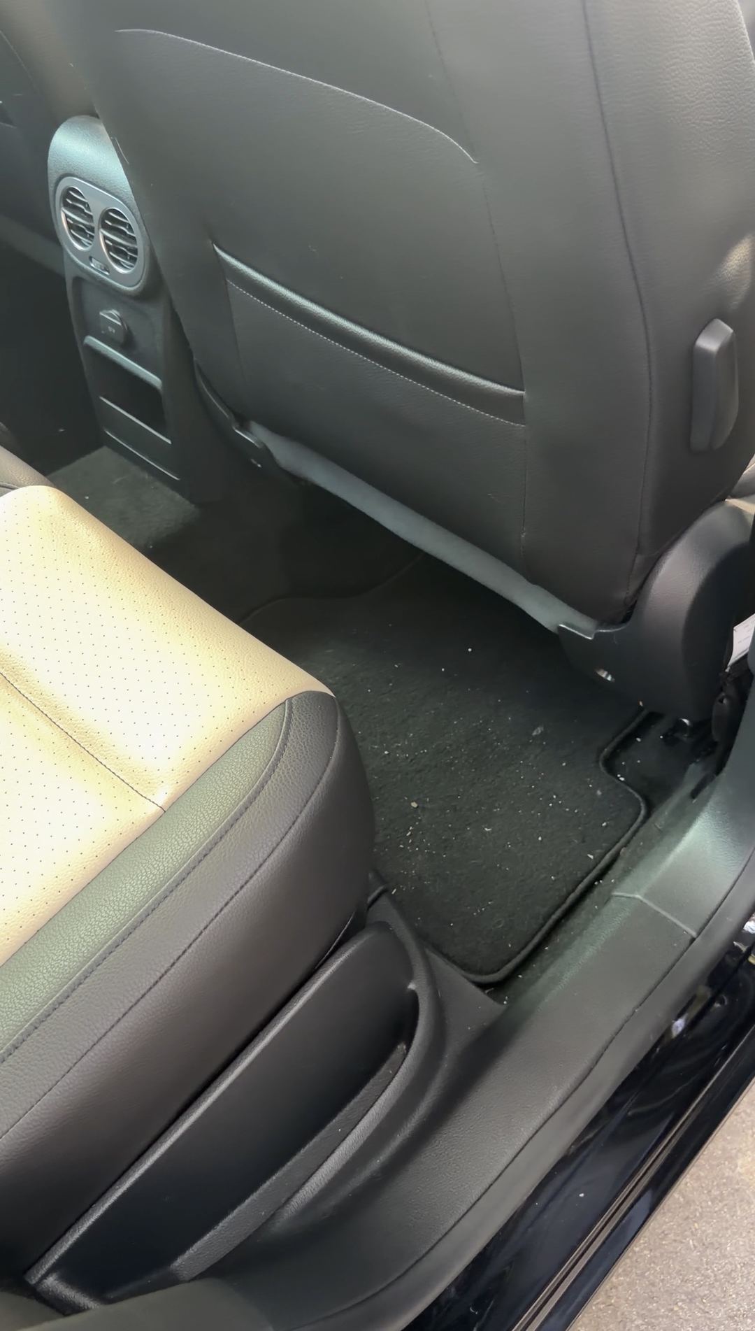Passenger-side rear footwell of a black VW Tiguan before detailing, crumbs on the rear floor mat.