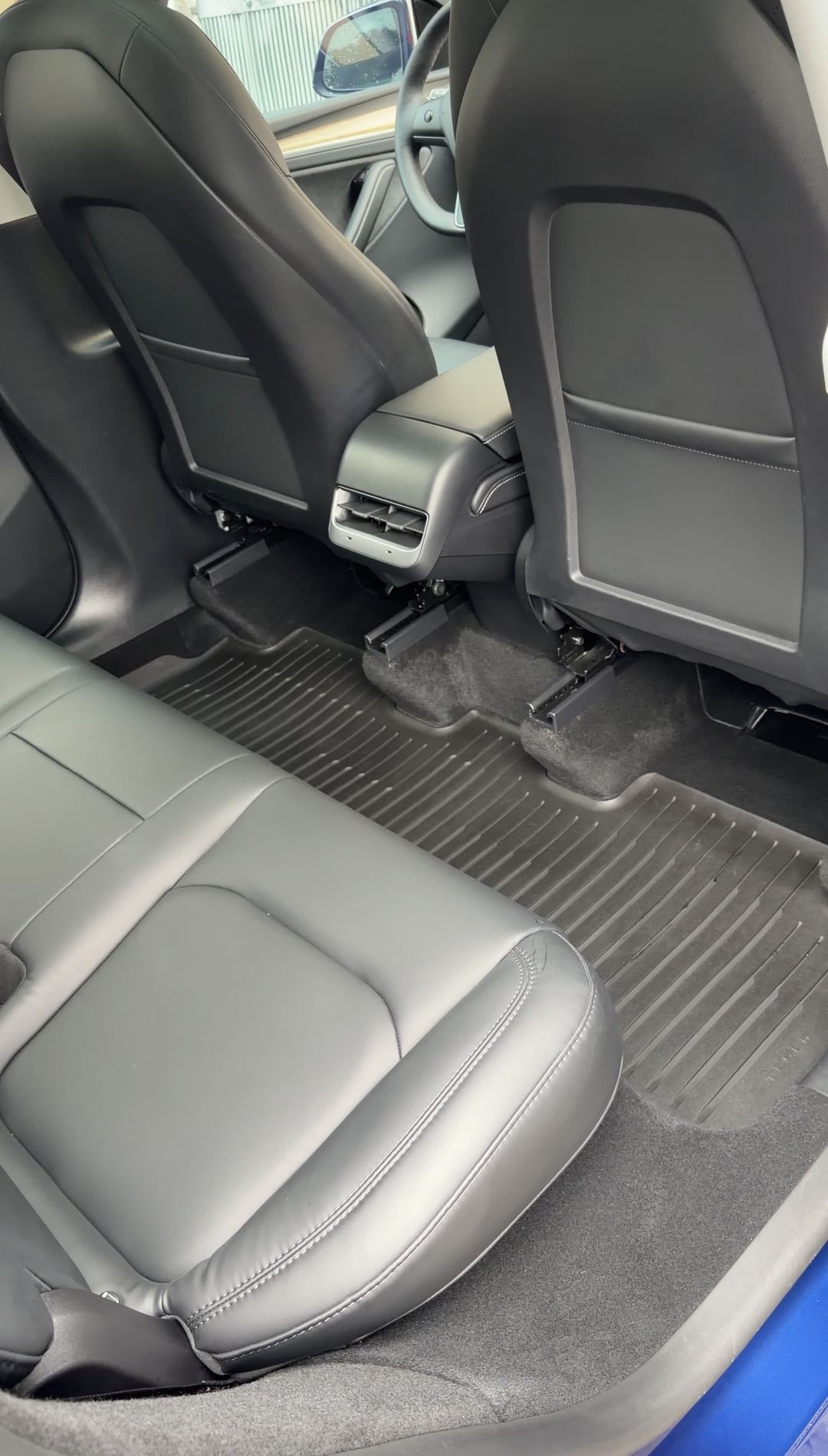 Clean rear passenger-side footwell of a Tesla Model Y with the floor liner refitted after detailing.