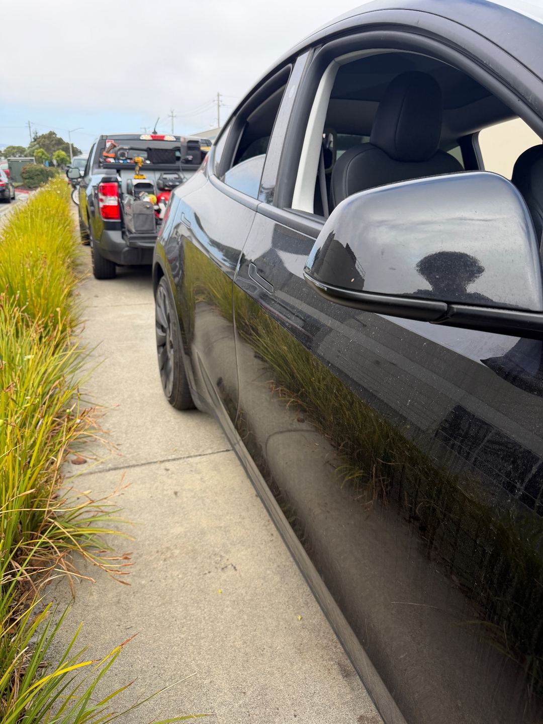 Side of a black Tesla Model Y before washing, with the detailing truck parked behind