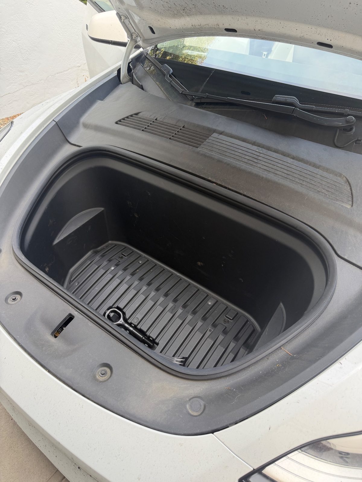 Front trunk of a white Tesla Model Y before detailing, with dust and grit around the liner