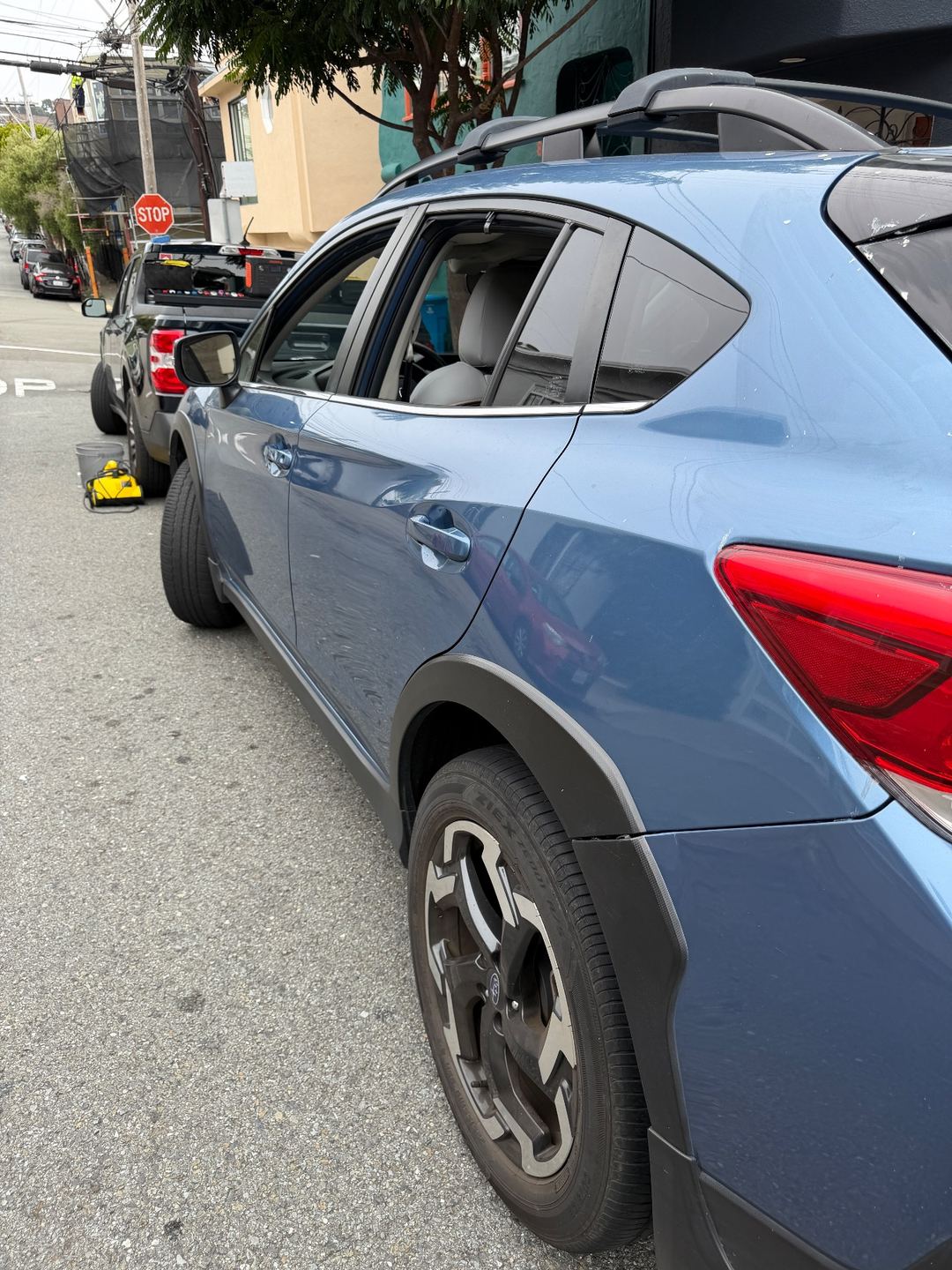 Left rear quarter of a blue Subaru Crosstrek before washing, with dust and white spots on the paint