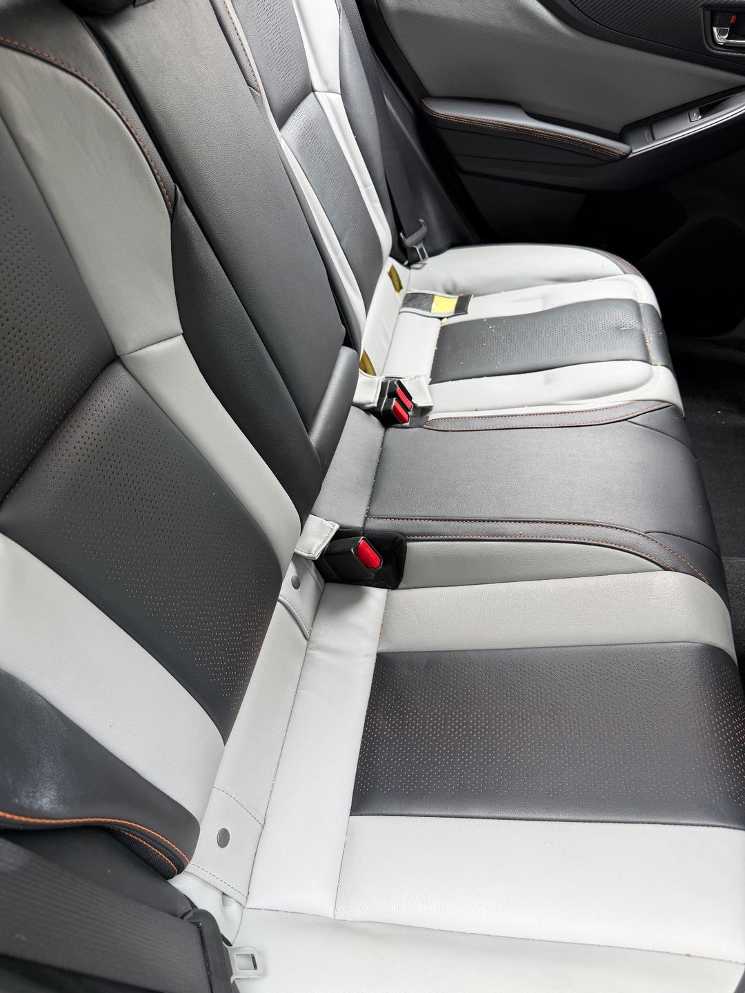 Rear bench seat of a Subaru Crosstrek before detailing, with dust and smudges on the grey and black leather