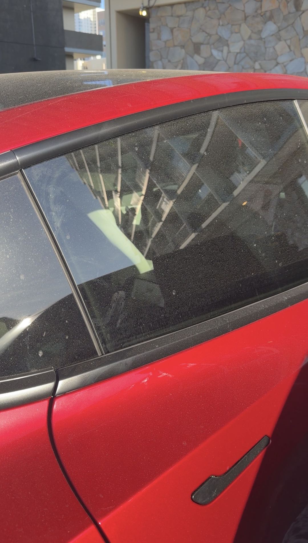 Dust-covered rear door glass and quarter window of a red Tesla Model Y before an exterior wash