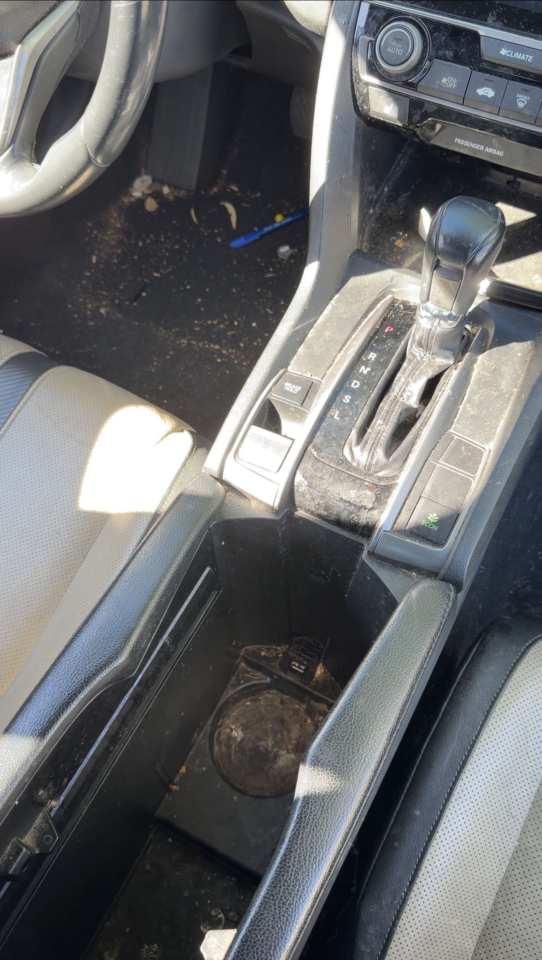 Centre console of a 10th-generation Honda Civic before cleaning, with caked brown residue in the cupholder wells and grit across the shifter gate