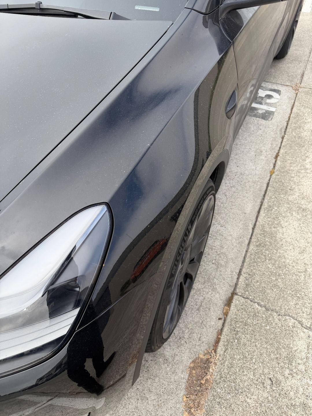 Left front fender and headlight of a black Tesla Model Y before washing, with dust and grime