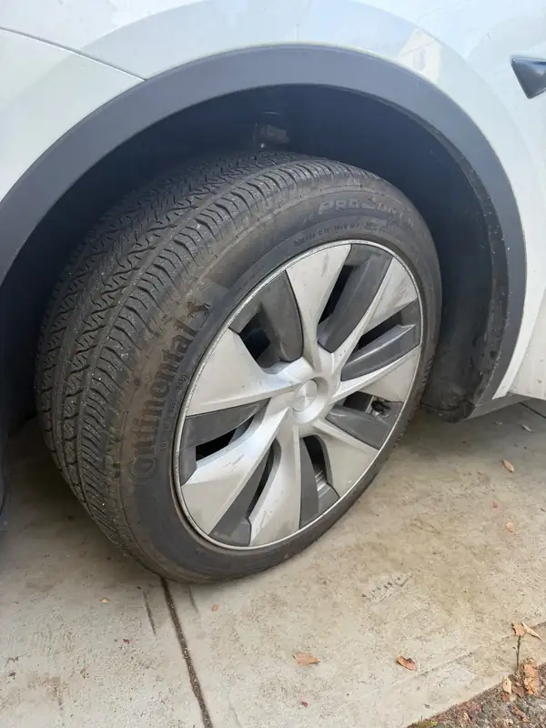 Front wheel of a white Tesla Model Y before detailing, with a brown film on the tyre and a grimy wheel cover