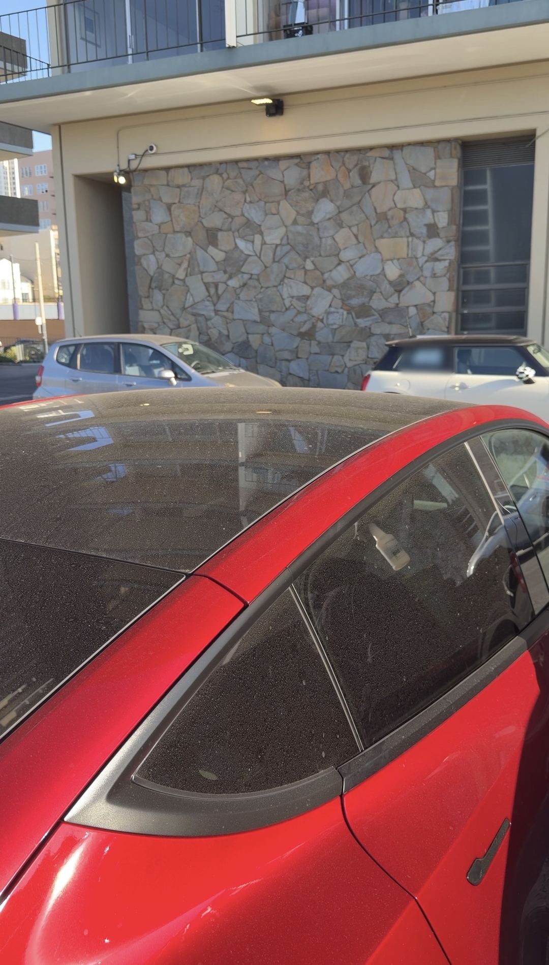 Dust-covered glass roof and side windows of a red Tesla Model Y in a parking lot before an exterior wash