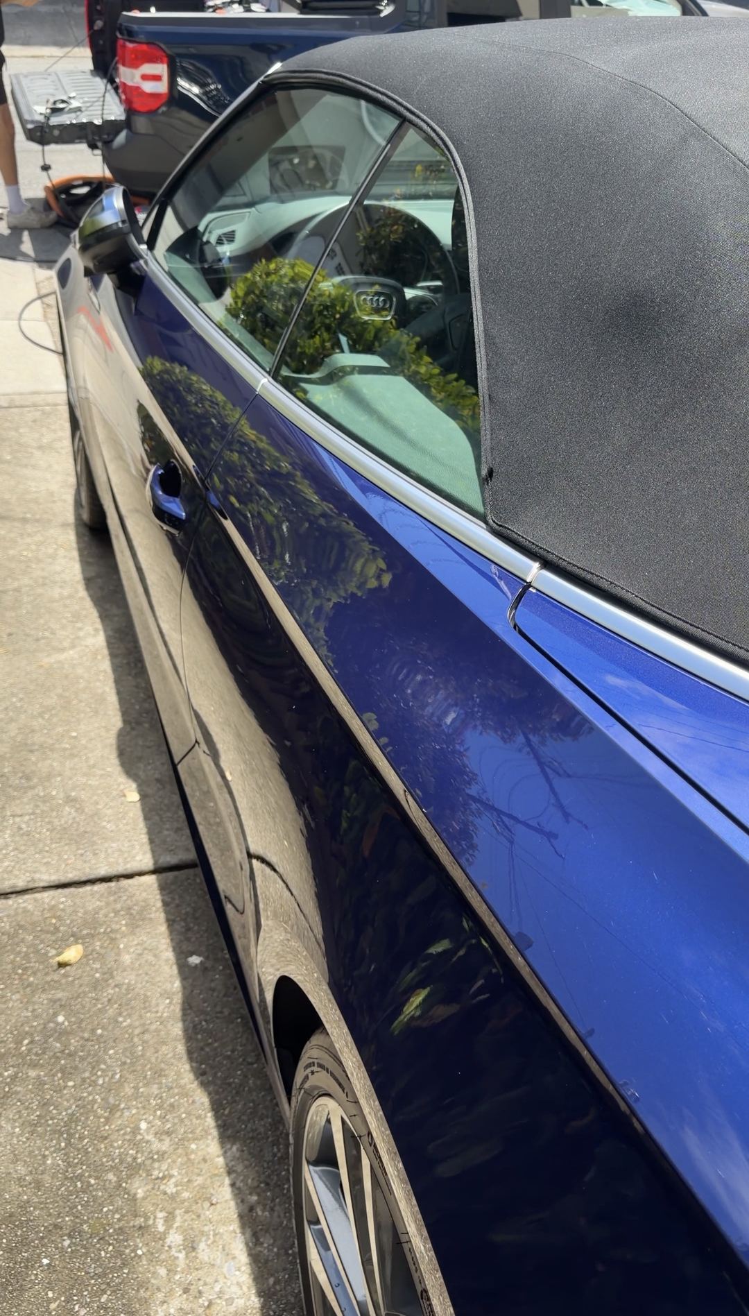 Side of a clean blue Audi S5 Cabriolet with detailing equipment on a truck behind
