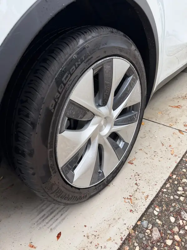 Front wheel of a white Tesla Model Y after detailing, with a black dressed tyre and a clean wheel cover