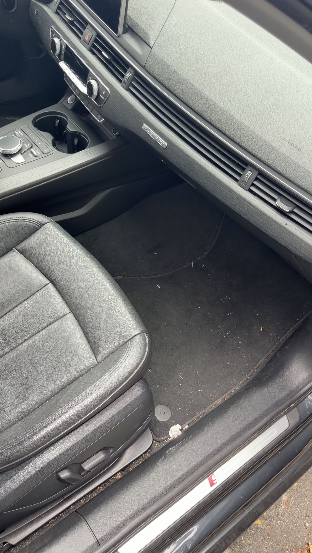 Dusty front passenger floor mat and sill of a grey Audi A4 with black leather seats