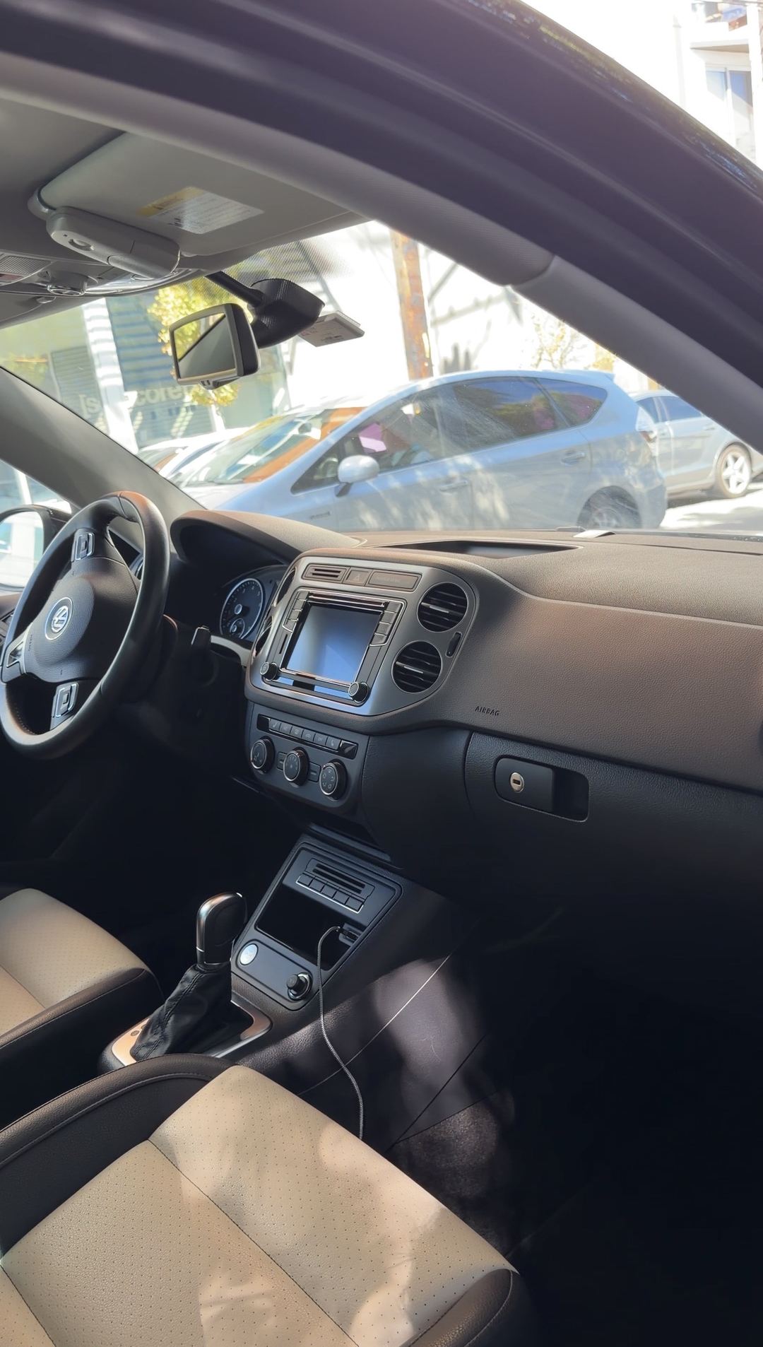 Interior of a black VW Tiguan after detailing, dashboard and beige front seats seen from the open passenger door.