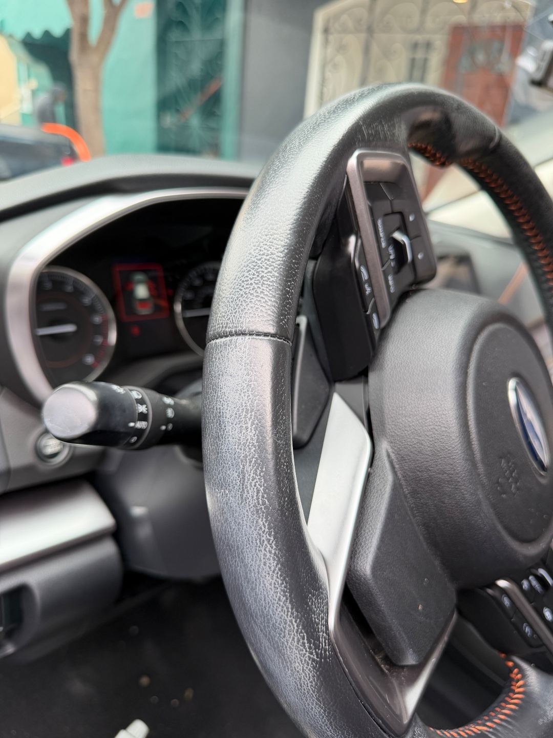 Steering wheel of a Subaru Crosstrek before detailing, with pale grime across the leather rim