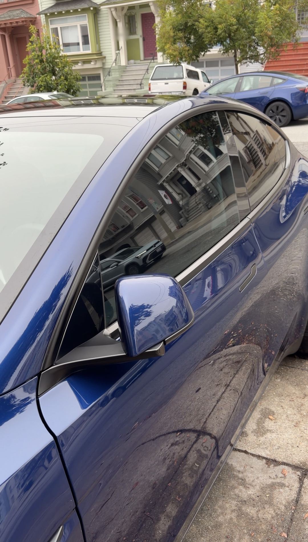 Mirror-finish reflection of a Victorian house in the clean door of a deep blue Tesla Model Y after detailing.