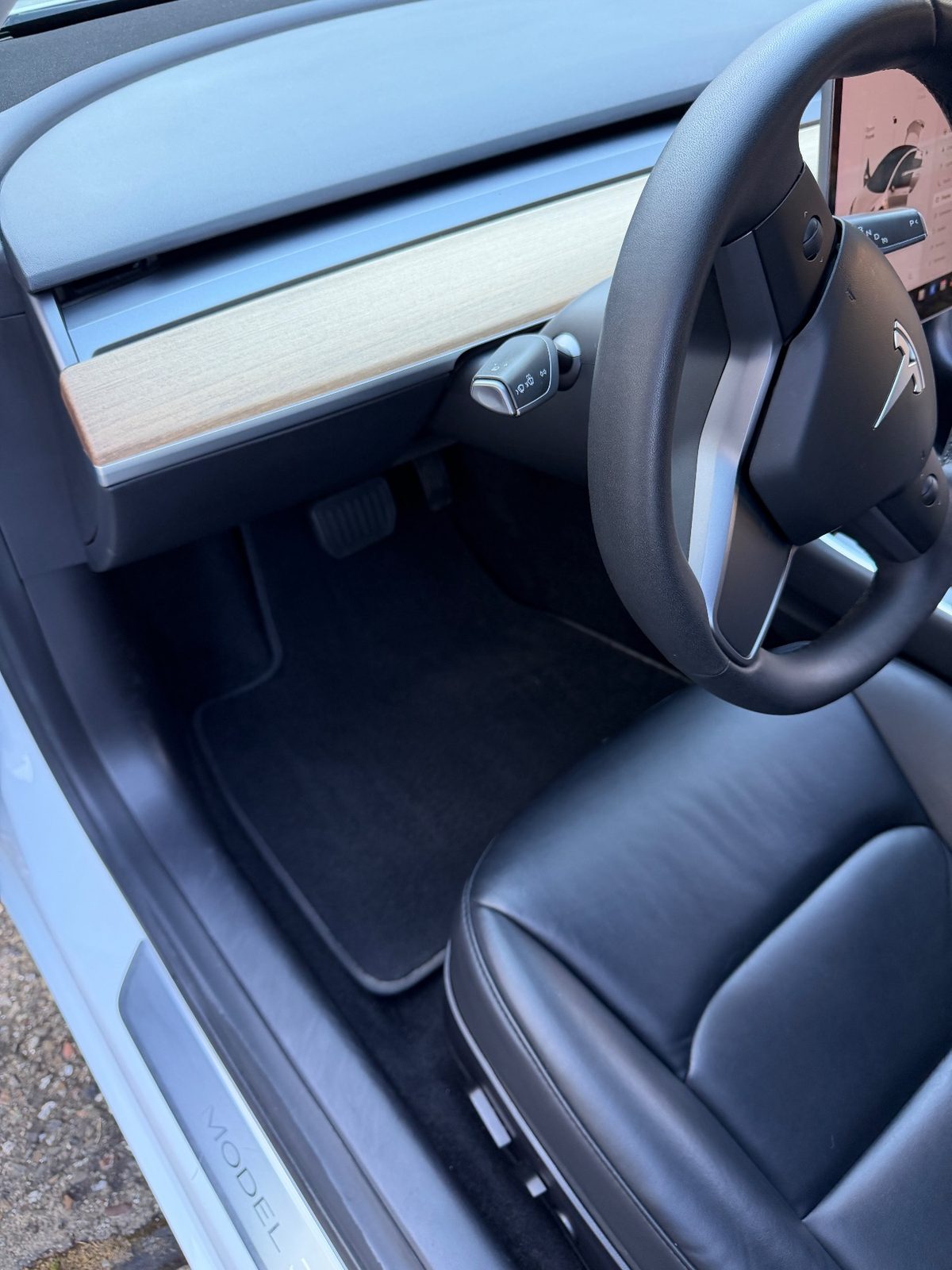 Driver footwell of a white Tesla Model 3 after detailing, with a clean vacuumed floor mat
