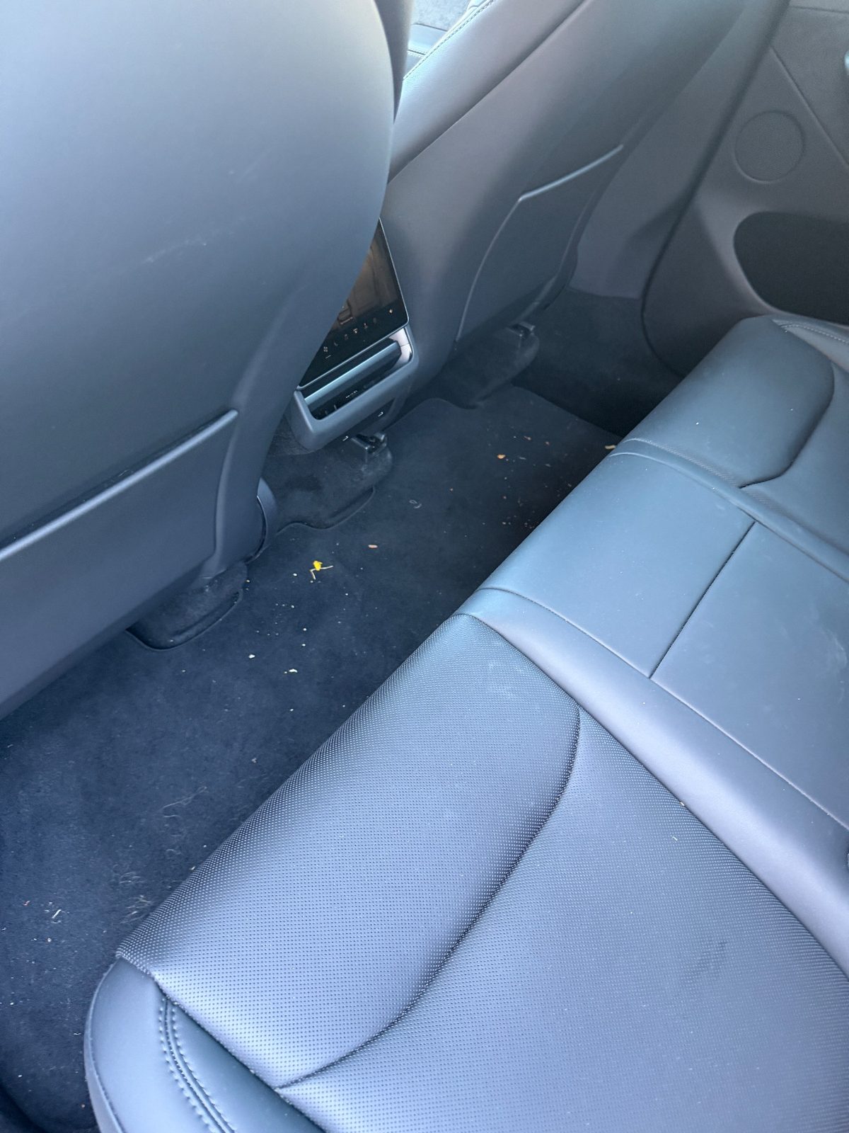 Rear footwell of a white Tesla Model Y before cleaning, crumbs and hair on the carpet