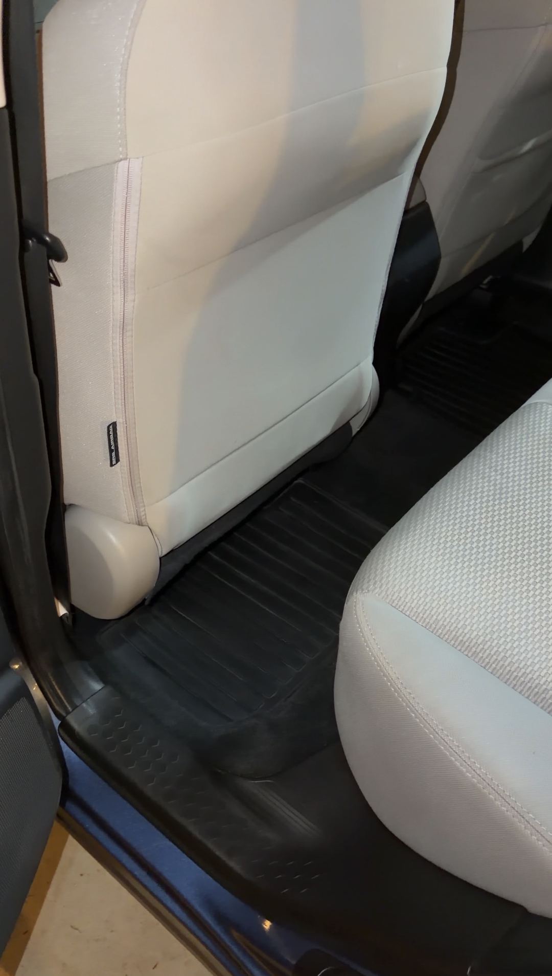 Rear driver-side footwell of a blue Subaru Forester after detailing, the black rubber mat clean with the leaf debris removed.