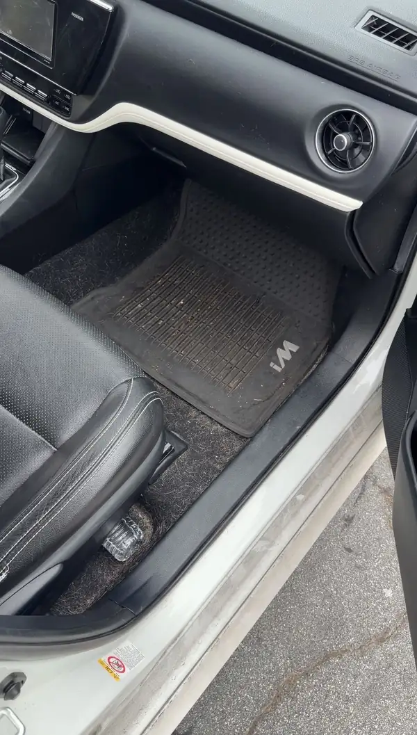 Front passenger footwell of a Toyota Corolla iM before cleaning, with a soiled iM-branded rubber liner and pet hair matted into the carpet beside it.